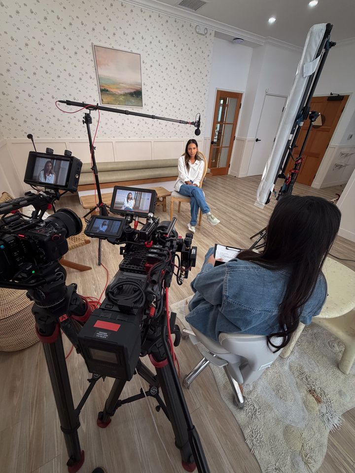 A wide view of the interview set: cameras, monitors, boom microphone and the interviewer with her question sheet